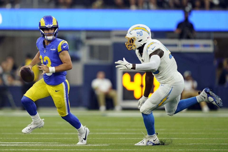 El mariscal de campo de los Rams, Stetson Bennett (13), corre desde el apoyador de los Chargers, Brevin Allen (90), en un partido de pretemporada.