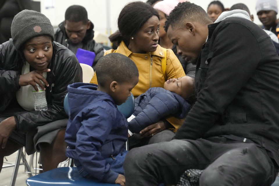 Petterly Jean-Baptiste, right, and his wife Leonne Ysnardin, behind center, both immigrants from Haiti, wait with their two children, Thursday, Nov. 16, 2023, at the Immigrant Family Services Institute, in the Mattapan neighborhood of Boston, for transportation to a shelter, in Quincy, Mass. Across the region, advocates relied on a patchwork of temporary shelters including churches, hospital waiting rooms and even airport lounges after Massachusetts' emergency shelter system hit a state-imposed limit of 7,500 families last week. (AP Photo/Steven Senne)