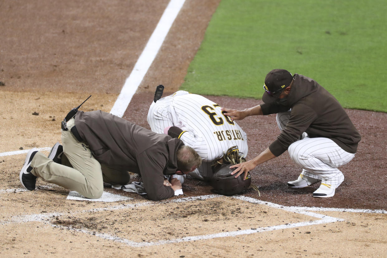 San Diego Padres manger Jayce Tingler, right, and a trainer, left, attend to Fernando Tatis Jr., center, after Tatis hurt his shoulder while swinging at a pitch in the third inning of a baseball game against the San Francisco Giants, Monday, April 5, 2021, in San Diego. (AP Photo/Derrick Tuskan)