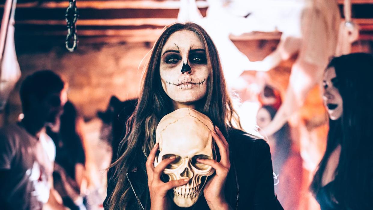 young woman with santa muerte make up and disguise holding skull at halloween party