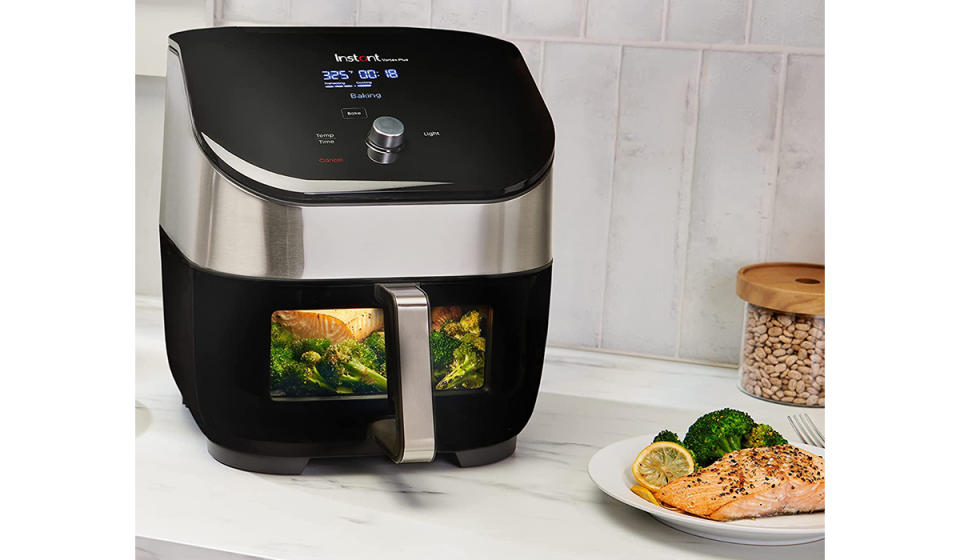 An air fryer with salmon and broccoli inside and outside