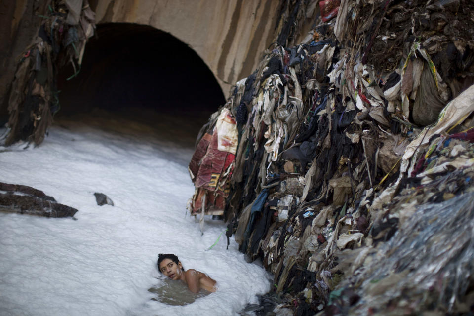 <p>In this photo taken on Wednesday Oct. 19, 2011, a youth who goes by the name Paleta searches for metal in contaminated water by a tunnel where the water from sewage converges with storm water runoff at the bottom of one of the biggest trash dumps in the city, known as “the Mine,” in Guatemala City. (Photo: Rodrigo Abd/AP) </p>