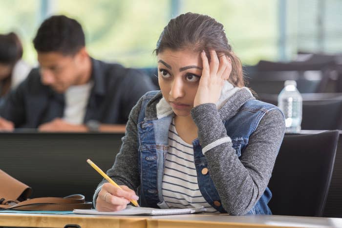 Student in a lecture hall looking pensive holding a pencil, denim jacket over striped shirt