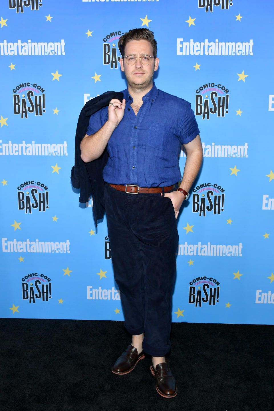 Trevor Einhorn wears blue shirt with black pants and jacket slung over his shoulder 