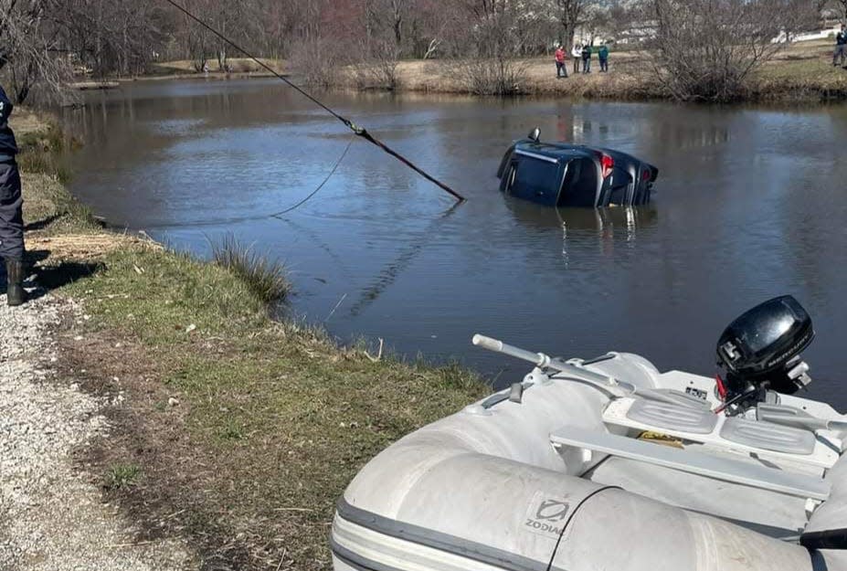 Residents watch as crews using a power winch to pull the car out of the pond