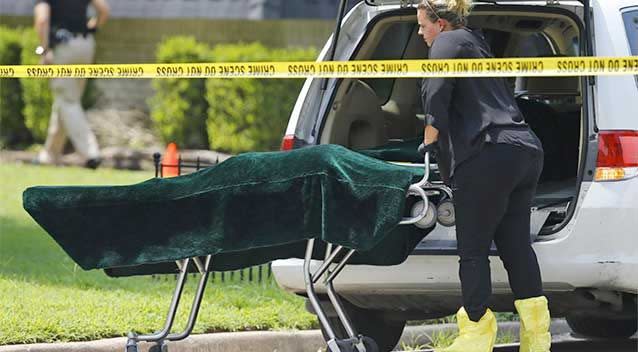 A worker wheels a gurney with a body bag on it, under the green cover, to a coroner's van outside of a home in Broken Arrow, Oklahoma. Photo: AP