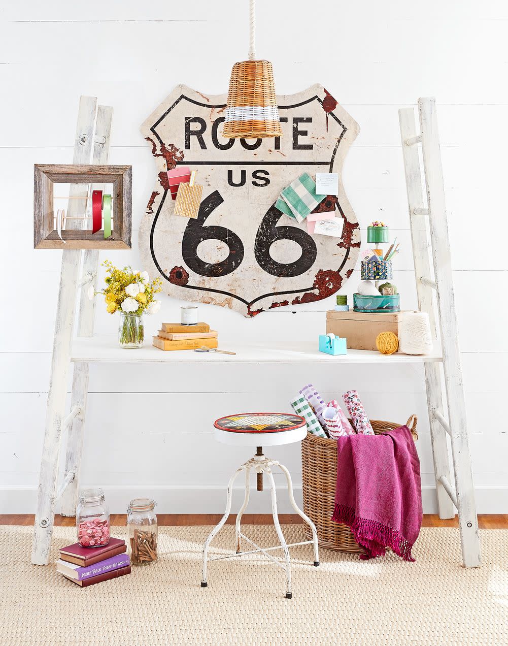 a white office with colorful sewing materials strewn about and a vintage route 66 sign hangs above the desk