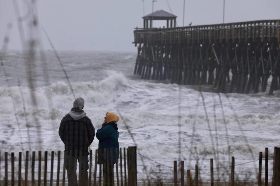 A couple on the beach watch Tuesday as waves batter against the 2nd Avenue Pier in Myrtle Beach as a severe storm begins lashing the Grand Strand area. Jan. 9, 2024