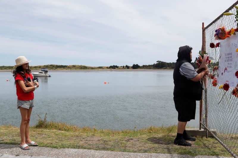 A girl watches as a man offers flowers at a memorial at the harbour in Whakatane, following the White Island volcano eruption in New Zealand