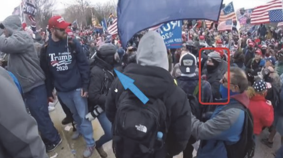 A screenshot of a video allegedly showing Peter Moloney, highlighted in red, advancing toward an Associated Press photographer, indicated by the blue arrow, on Jan. 6, 2021.  / Credit: Justice Department