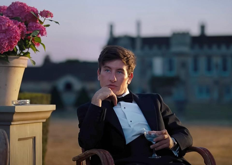 Barry in a tux sitting in a chair outdoors in a scene from "Saltburn"