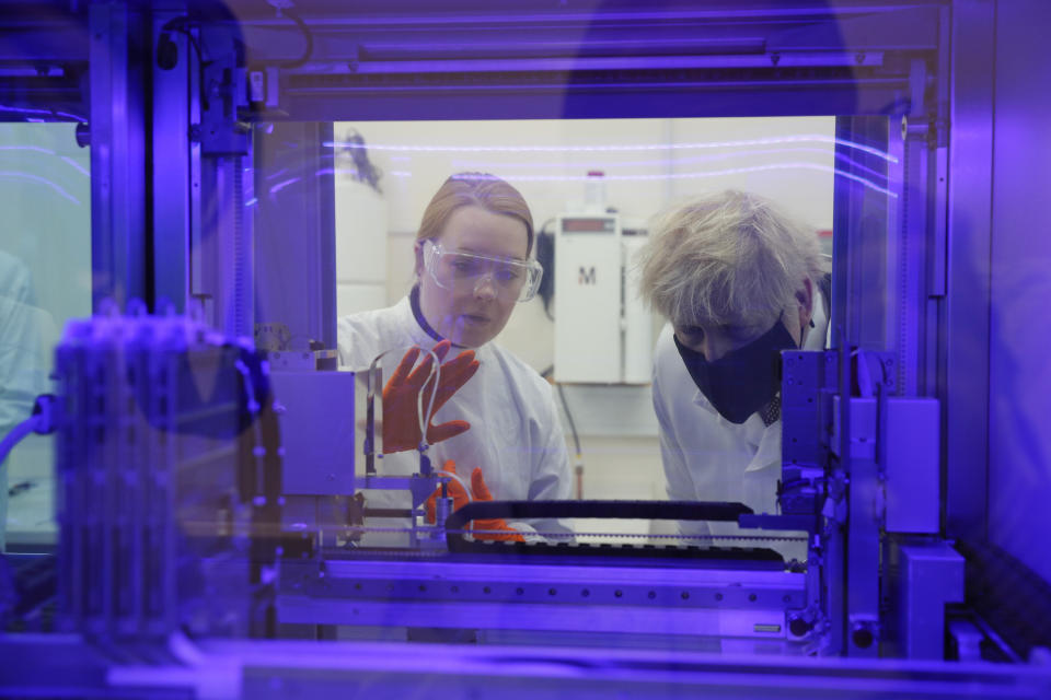 Britain's Prime Minister Boris Johnson views a PCR diagnostics machine with biomedical scientist Jodie Owen, left, in a laboratory during a visit to the Public Health England site at Porton Down science park near Salisbury, southern England, on Friday Nov. 27, 2020. (Adrian Dennis/Pool via AP)