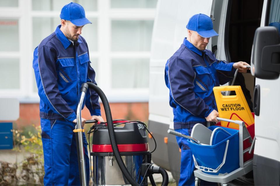 Two men unload cleaning equipment from a truck.