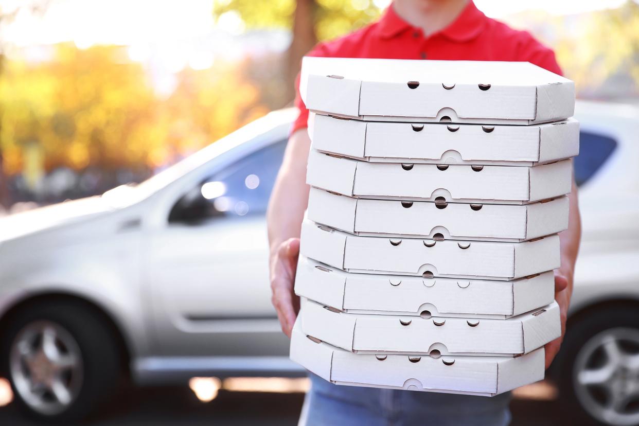 pizza delivery boy holding several boxes with pizza near car
