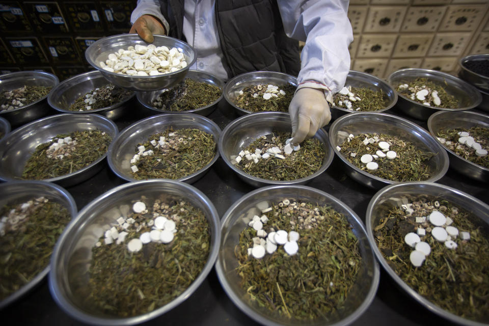 In this March 13, 2020 photo, a worker assembles ingredients for traditional Chinese medicine preparations into bowls at the Bo Ai Tang traditional Chinese medicine clinic in Beijing. With no approved drugs for the new coronavirus, some people are turning to alternative medicines, often with governments promoting them. (AP Photo/Mark Schiefelbein)