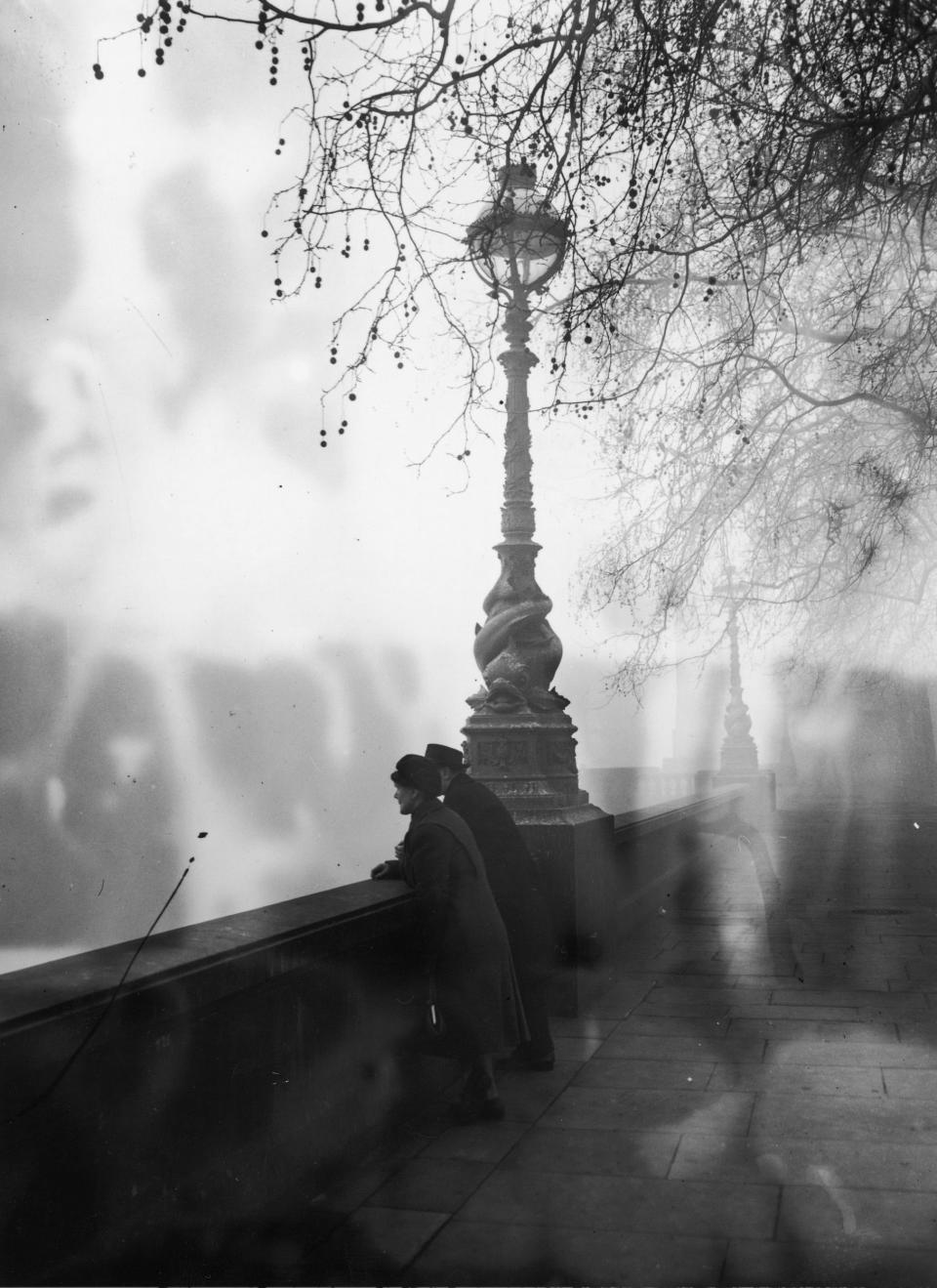 People standing near a lampost of an embankment are covered by smog on December 5, 1952, in Blackfriars, London.