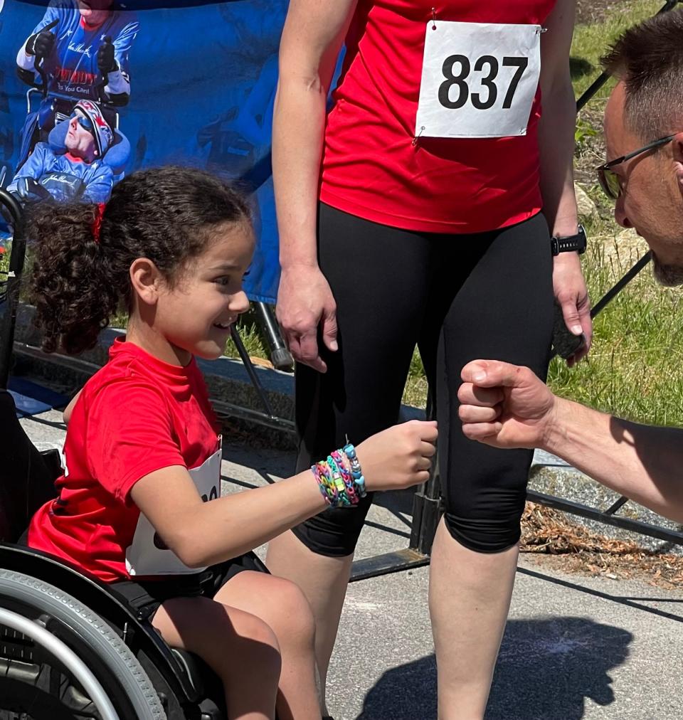 Ellie Moore, 11, of Dudley receives a fist bump from Rick Hoyt’s brother, Russ, after finishing the inaugural Dick Hoyt Memorial Yes You Can Race in Hopkinton on Saturday.