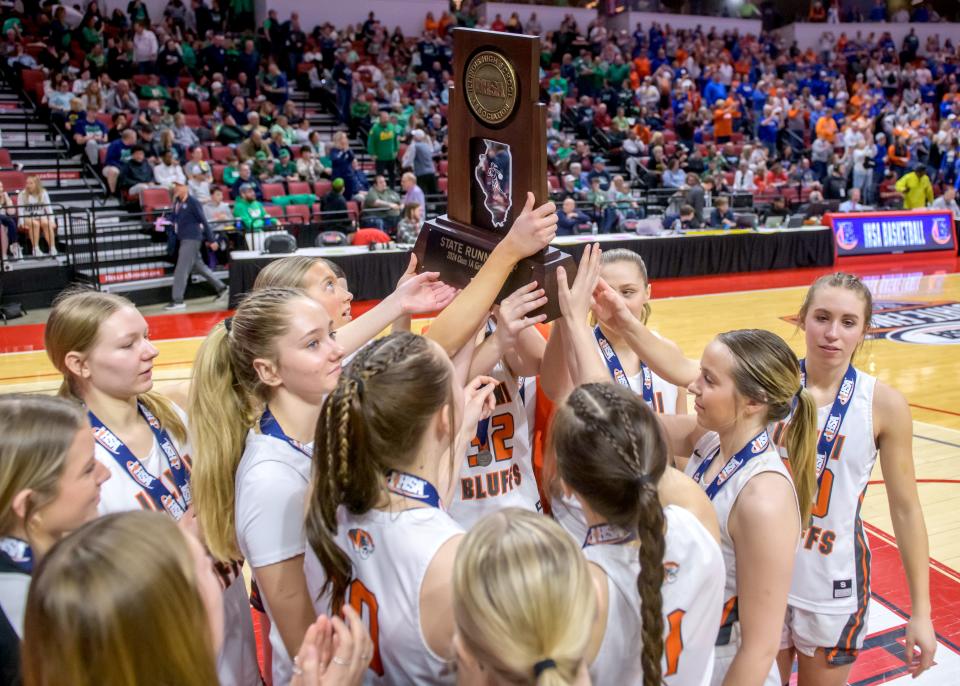 The Illini Bluffs Tigers gather around their Class 1A girls basketball state runner-up trophy after falling 48-36 to defending champ Okawville in the title game Saturday, March 2, 2024 at CEFCU Arena in Normal.