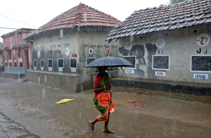 A woman holding an umbrella walks past houses with the walls converted into black boards that children use during their open-air classes at Joba Attpara village