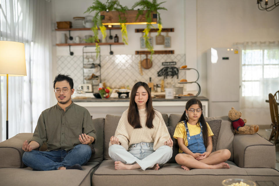 Family sitting on a couch and meditating indoors (Photo: Getty Images)