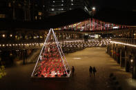 FILE - In this Monday, Nov. 23, 2020 file photo, people walk past the 'Terrarium Tree' in Coal Drops Yard, which forms part of the King's Cross neighbourhood of London's unconventional Christmas tree installations, during England's second coronavirus lockdown. Nations are struggling to reconcile cold medical advice with a holiday tradition that calls for big gatherings in often poorly ventilated rooms, where people chat, shout and sing together, providing an ideal conduit for a virus that has killed over 350,000 people in Europe so far. (AP Photo/Matt Dunham, FIle)