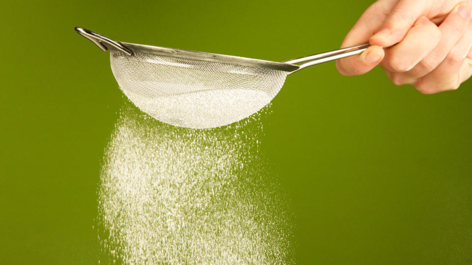 Sieve and powdered sugar on orange background.