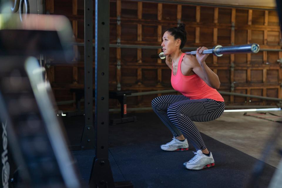 A woman squatting with an empty barbell in a garage gym.