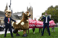 A man imitates the injection of hormones into a man in a cow costume, in Parliament Square, as part of a day of action against the US trade deal, ten days before the US Presidential election, in London, Saturday, Oct. 24, 2020. There will will be protests held nationwide against a proposed US trade deal, opposed by a number of organisations including Global Justice Now and Stop Trump Coalition. (AP Photo/Alberto Pezzali)