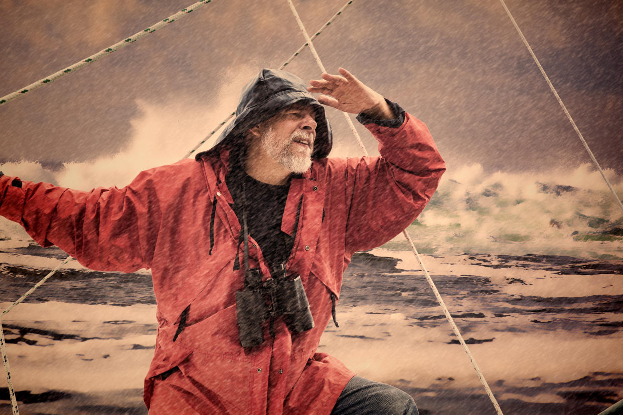 A man on the bow of a sailboat overlooks the a rough sea during a storm. (Filtered Image)