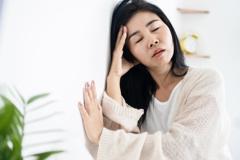 Asian woman having problem with Meniere's disease, fainting or dizziness hand holding her head leaning against the wall