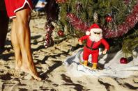 A surfing Santa decoration is placed under a Christmas tree in the sand as Staci Kennedy, of Cape Cod, Massachusetts, places a garland on the tree on Waikiki Beach in Honolulu, Hawaii December 25, 2013. Kennedy and her friends have been taking part in this Christmas day festivity for 16 years. REUTERS/Kevin Lamarque (UNITED STATES - Tags: SOCIETY RELIGION)