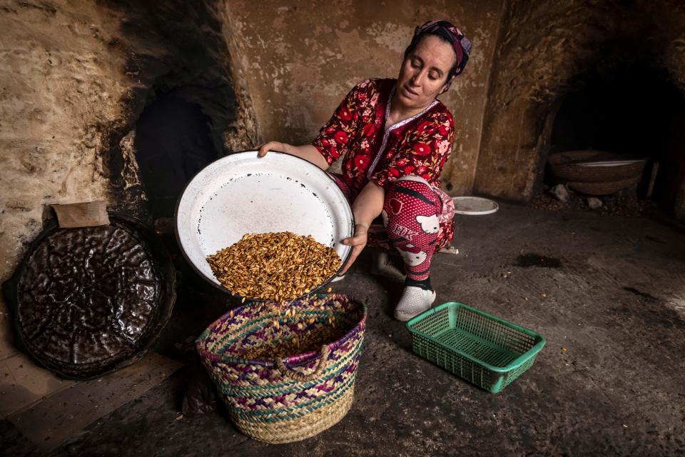 A woman empties roasted Argan nuts into a basket as she makes oil, at a house near Morocco's western Atlantic coastal city of Essaouira, on October 15, 2022. - Morocco's argan oil is highly prized by the cosmetics industry, yet it is now mostly produced by elderly workers, raising questions about how long the artisanal practice can continue. (Photo by FADEL SENNA / AFP) (Photo by FADEL SENNA/AFP via Getty Images)