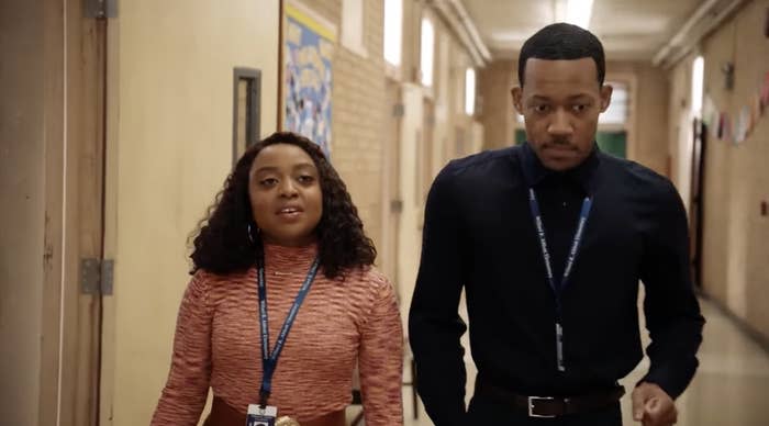 Janine and Gregory from Abbott Elementary School walk down the school hallway.A woman wearing a ribbed top and a man wearing a shirt and tie