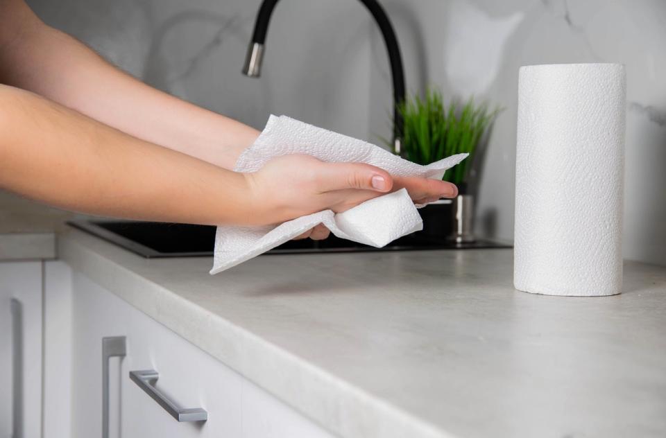 Wiping hands with paper towel next to sink with towel roll on kitchen counter