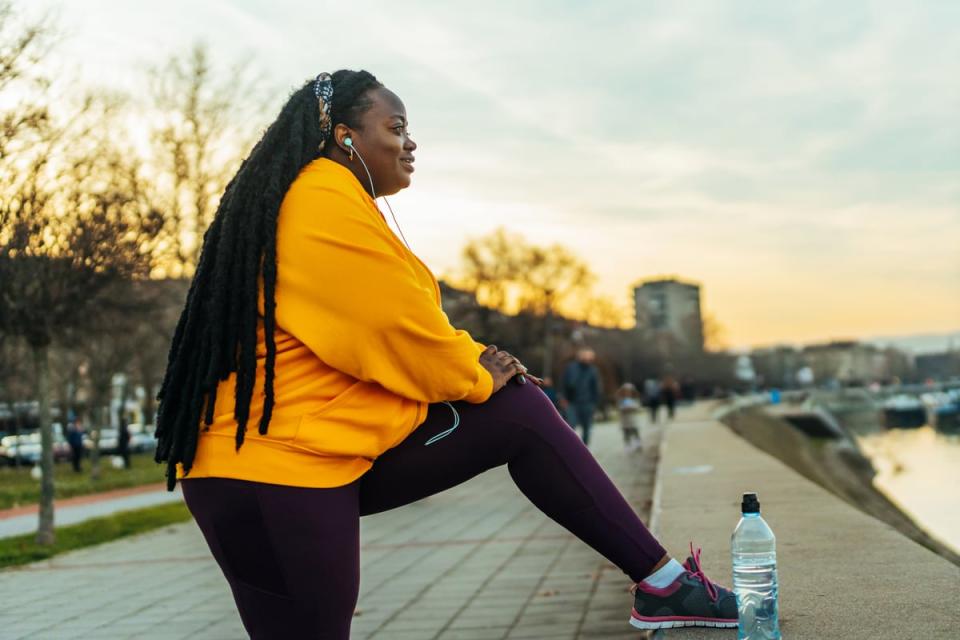 A person smiles while listening to music and stretching on a sidewalk. 