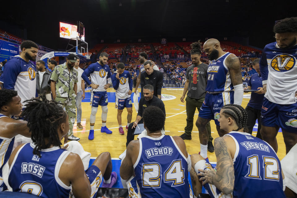 Bayamón Vaqueros players huddle with their coach during a time out in a game against the Guaynabo Mets at the Ruben Rodríguez Coliseum in Bayamón, Puerto Rico, Monday, July 1, 2024. Puerto Rico’s professional basketball league is experiencing a renaissance thanks to reggaeton stars like Bad Bunny, Ozuna and Anuel AA, who are stepping into the financial game, buying local teams and helping to stack up a loyal fan base. (AP Photo/Alejandro Granadillo)