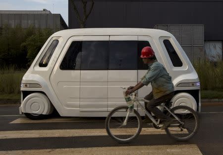A worker rides a bike past a driverless vehicle at Vanke's Building Research Centre testing area in Dongguan, south China's Guangdong province November 2, 2015. REUTERS/Tyrone Siu
