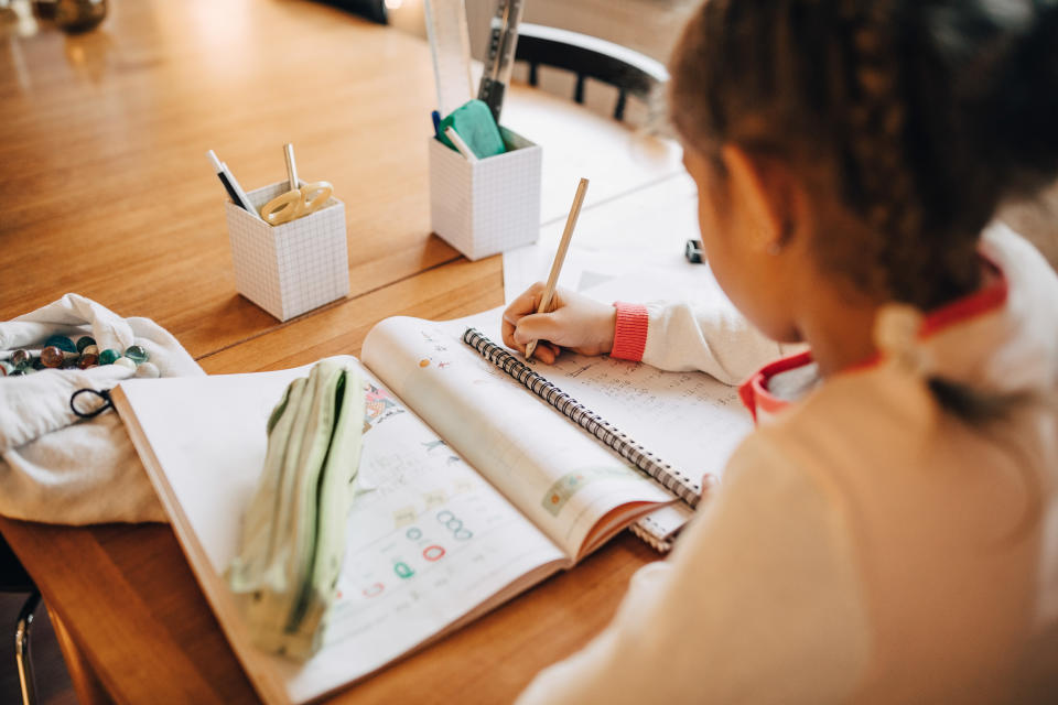 Rear view of girl writing homework on table while sitting at home