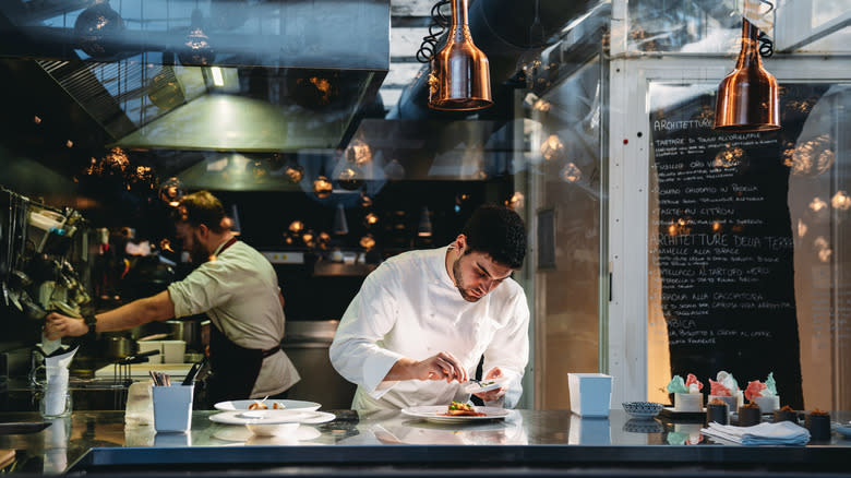 Chef in white coat putting finishing touches on plate of food