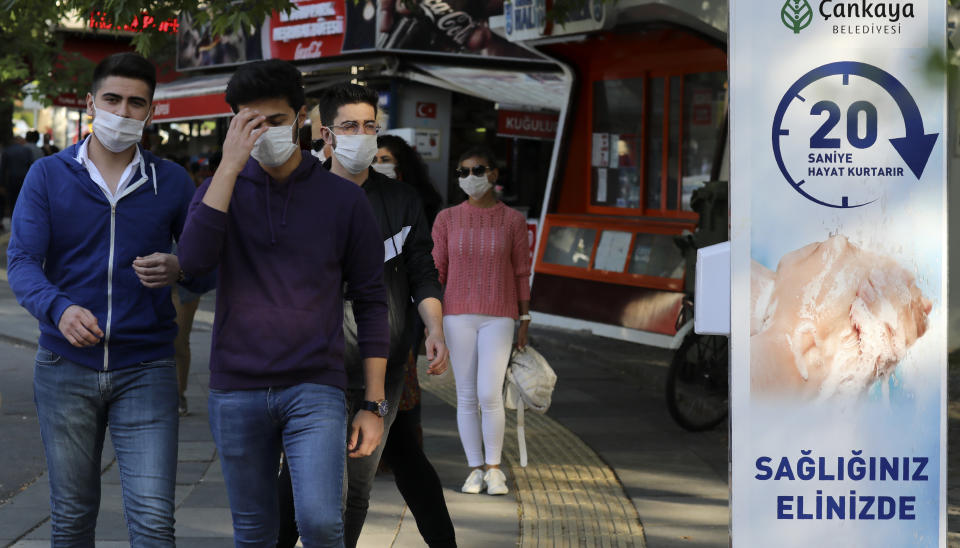 People wearing face masks to protect against the coronavirus, pass a sign that reads: "washing hands for 20 seconds saves your life", at the entrance of a public garden, in Ankara, Turkey, Sunday, June 14, 2020. Turkey's President Recep Tayyip Erdogan has revealed Tuesday new plans to ease restrictions in place to curb the spread of the coronavirus, including the July 1 reopening of theaters, cinemas and other entertainment centers. (AP Photo/Burhan Ozbilici)