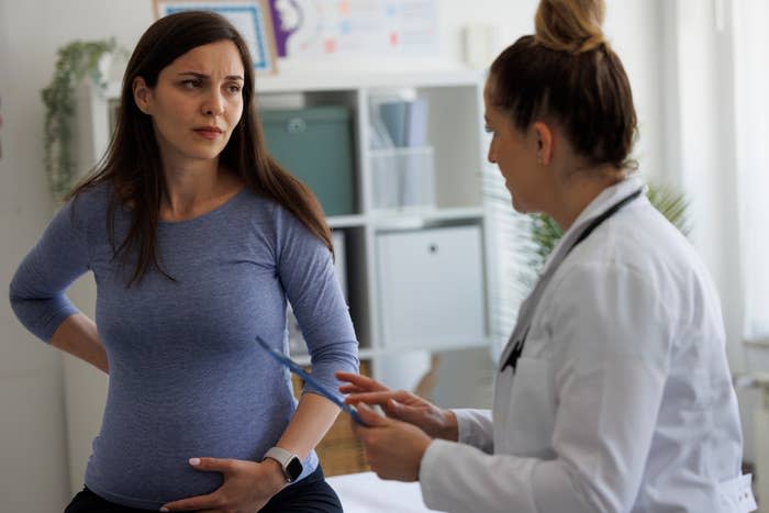 Pregnant woman consults with a doctor in an office setting. The woman is in casual attire, while the doctor wears a white coat. 