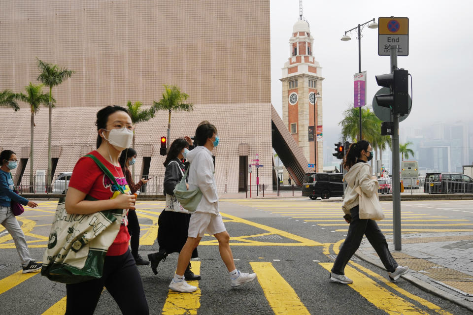 People wearing face masks walk along a street in Hong Kong, Friday, Jan. 28, 2022. Hong Kong is cutting the length of mandatory quarantine for people arriving from overseas from 21 to 14 days, even as the southern Chinese city battles a new surge in COVID-19 cases. (AP Photo/Kin Cheung)