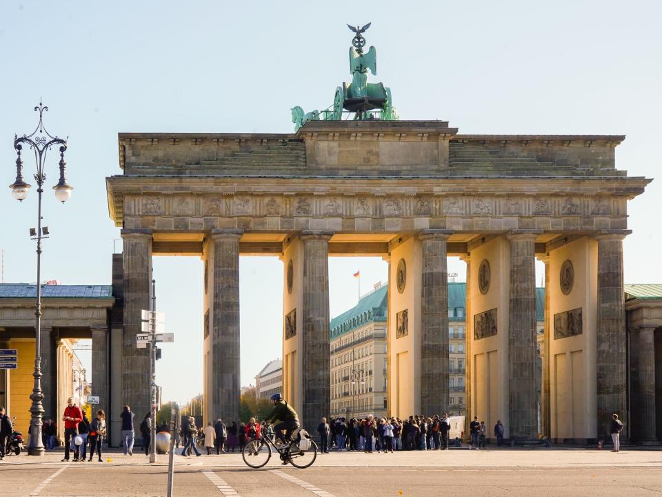 Sunlight peers through Brandenburg Gate in Berlin with people walking and biking on the street in front of it