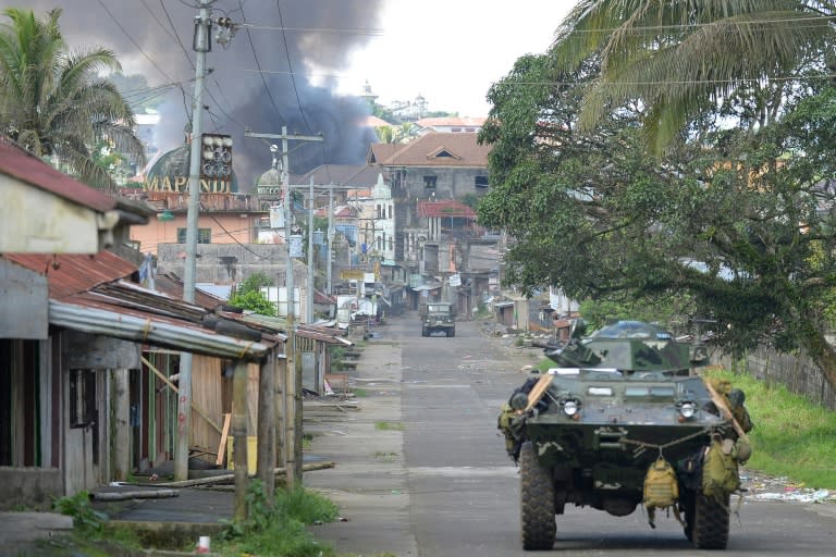 A Philippine Marines truck and armoured personnel carrier speed away as black smoke billows from burning houses after military helicopters fired rockets at militant positions in Marawi on the southern island of Mindanao