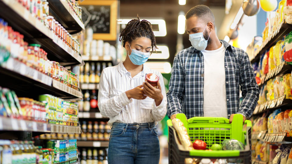 African Family Couple In Shop Buying Groceries Wearing Face Mask Choosing Food Goods Walking With Shopping Cart In Supermarket Store. Customers Buy Essentials During Pandemic. Panorama, Free Space