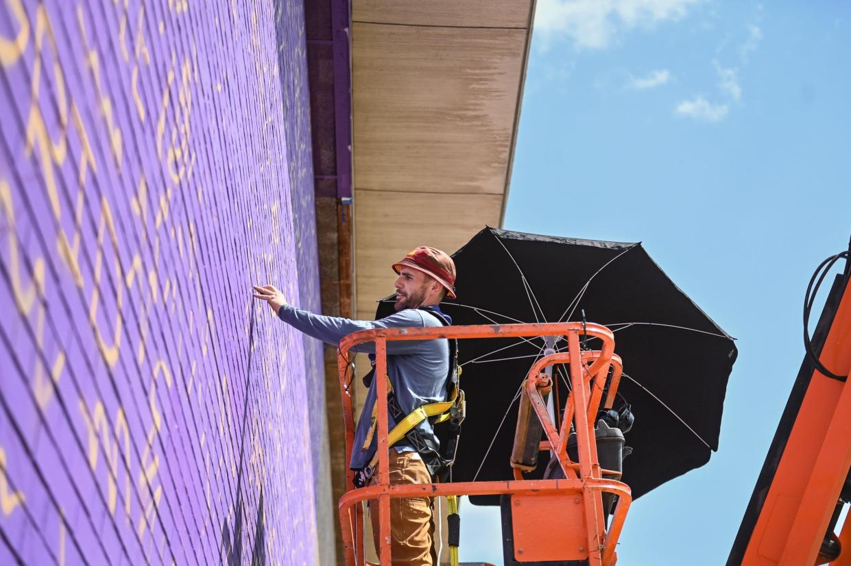 Artist Dustin Hunt of Muralmatics demonstrates one of the steps in his mural-making process, Wednesday, Aug. 14, 2024, at the Alfreda Schmidt Community Center on Lansing's southside. His three-part project titled "Lansing Shaped" will depict three generations of a Lansing family - children, parents, and grandparents, at three different schools.