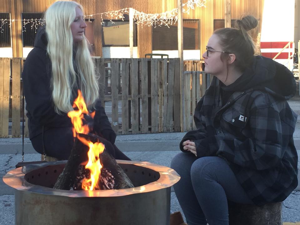 Marissa Hardman and Kennedy Davidson, both of Shelby, sit by a fire pit Thursday at Christmas in the Village in Plymouth.