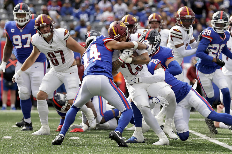 Washington Commanders running back Chris Rodriguez Jr. (23) is tackled by New York Giants cornerback Nick McCloud (44) and safety Jason Pinnock (27) during the third quarter of an NFL football game, Sunday, Oct. 22, 2023, in East Rutherford, N.J. (AP Photo/Adam Hunger)