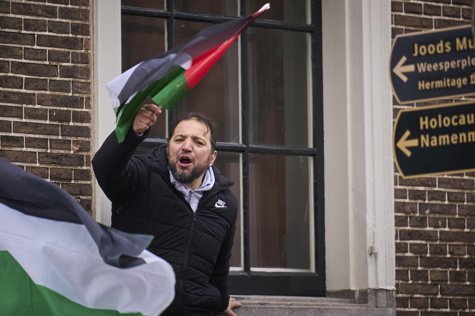 A man waves a Palestinian flag next to signs for the Holocaust Monument and the Jewish Museum as demonstrators protested against Israel's President Isaac Herzog attending the opening of the new National Holocaust Museum in Amsterdam, Netherlands, Sunday, March 10, 2024. (AP Photo/Phil Nijhuis)