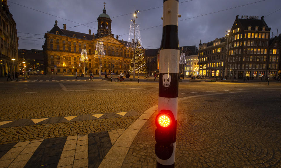 FILE- In this Tuesday Dec. 15, 2020, file photo, A skull is glued onto a traffic light on the near-empty Dam Square with the Royal Palace, seen center rear, in Amsterdam, Netherlands. The Dutch government said Wednesday, Jan. 20, 2021, that it wants to impose a curfew as part of beefed-up restrictions to rein in the spread of new more contagious variants of the coronavirus that already accounts for at least one in every 10 Dutch infections.(AP Photo/Peter Dejong, File)